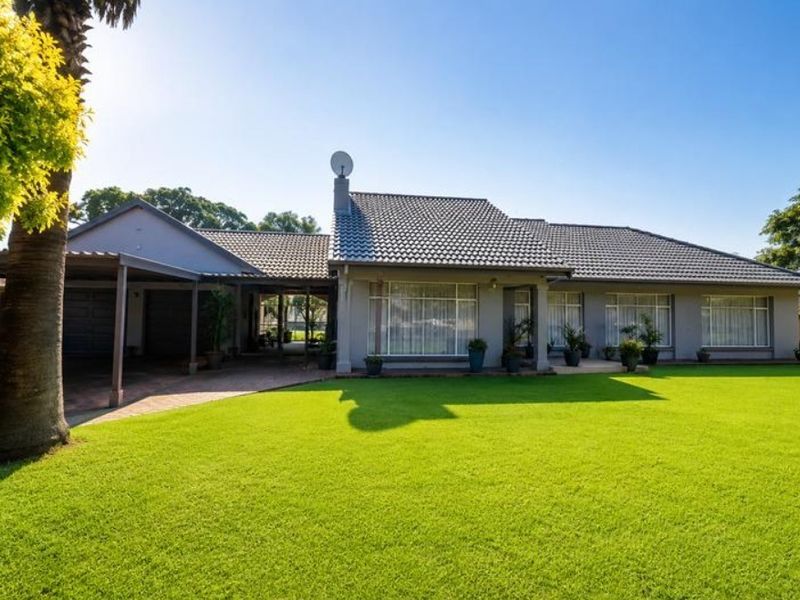 A well-maintained single-story house featuring a tiled roof, a spacious front lawn, and an attached covered carport with a paved driveway.