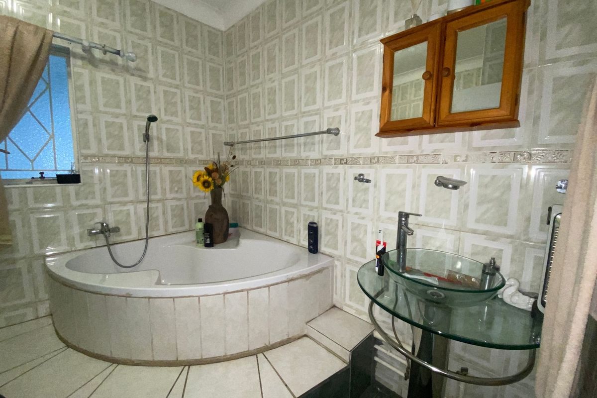 Bathroom featuring a corner bathtub with handheld shower, glass vessel sink on a pedestal, and full-height ceramic wall tiling.
