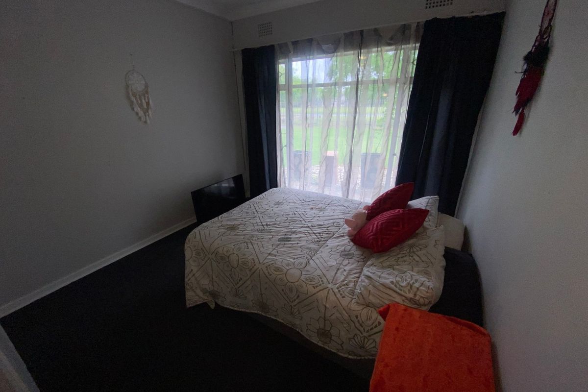 A bedroom featuring a large window with curtains and a ceiling ventilation vent, providing natural light and airflow.