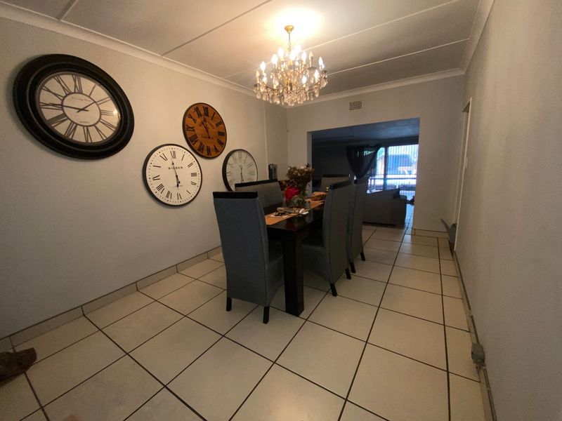 A dining room featuring tiled flooring, ceiling coving, and a central chandelier, leading into an adjacent living area.