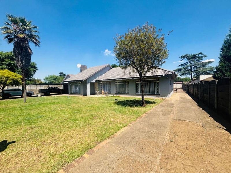 Front view of a single-story house featuring a tiled roof, concrete driveway, carport, and a spacious front garden with perimeter walling.