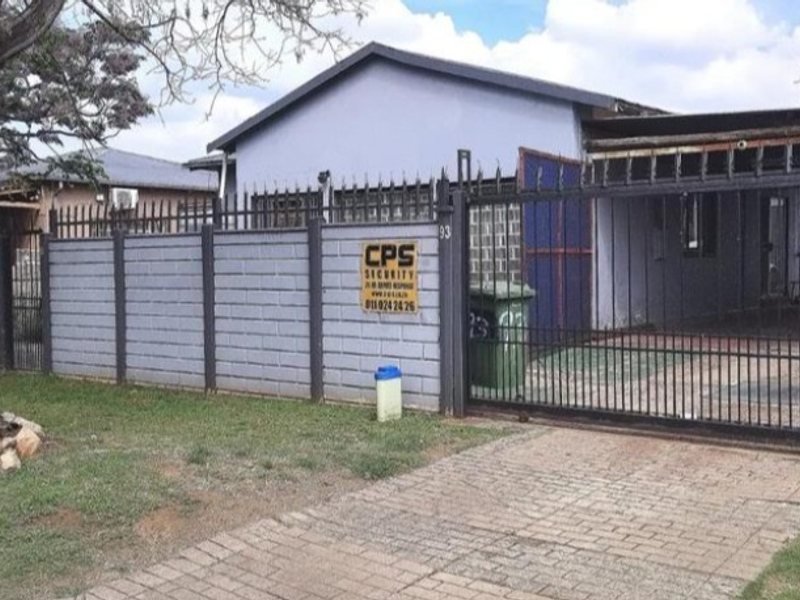 Front view of the property featuring a paved driveway, secure metal gate, and perimeter walling.