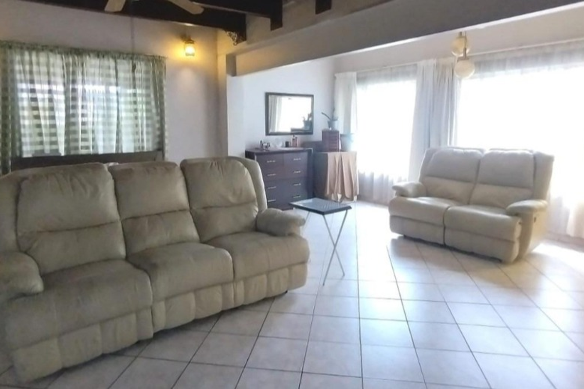 Spacious living room featuring ceramic floor tiles, exposed timber ceiling beams, and a ceiling fan, offering a comfortable and functional living space.