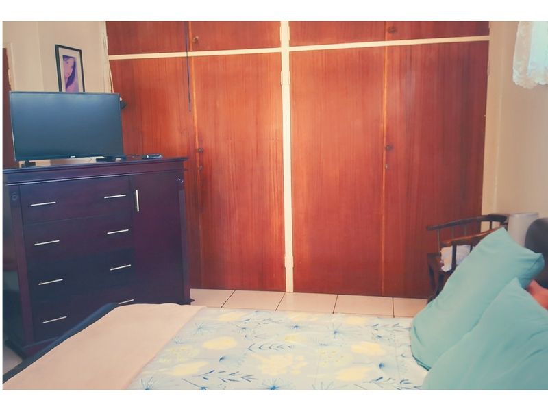 A bedroom featuring built-in wooden cupboards and tiled flooring.
