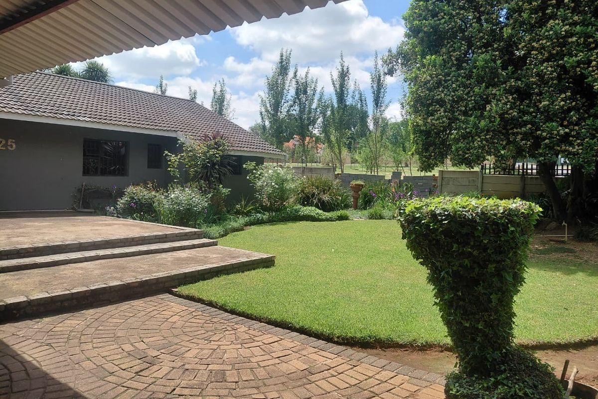 A well-maintained rear garden featuring a paved patio area, concrete steps, and a lush lawn, bordered by a precast concrete boundary wall.