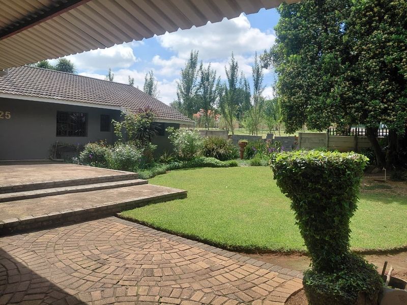 A well-maintained rear garden featuring a paved patio area, concrete steps, and a lush lawn, bordered by a precast concrete boundary wall.
