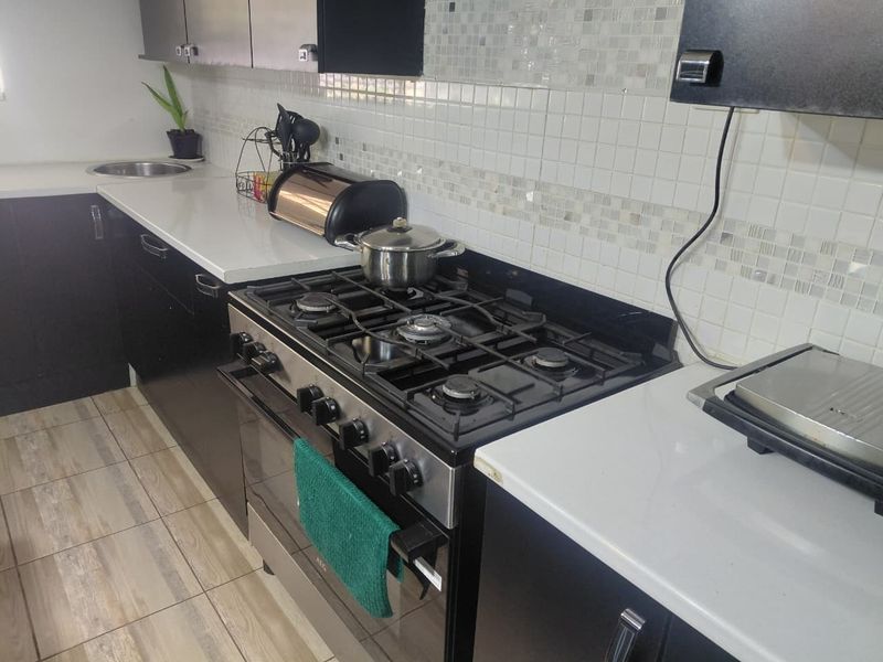 A functional kitchen featuring dark cabinetry, white quartz countertops, a gas stove with oven, and a decorative mosaic tile backsplash.