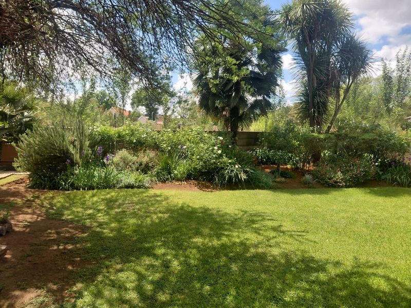 A well-maintained private garden featuring a lush green lawn, mature trees, and established perimeter garden beds with a boundary wall.
