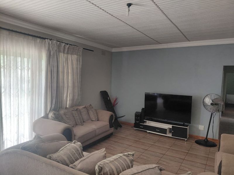 A living room featuring tiled flooring, a coved ceiling, and a sliding glass door with security gate providing access to the exterior.