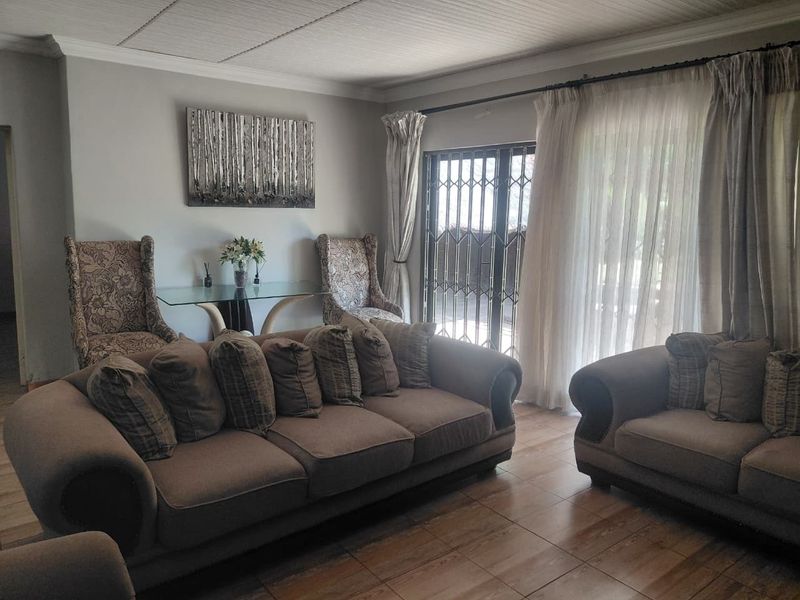 A comfortable living room featuring tiled flooring, crown molding, and a sliding glass door with a security gate leading to the exterior.