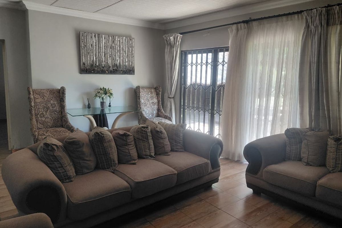 A comfortable living room featuring tiled flooring, crown molding, and a sliding glass door with a security gate leading to the exterior.