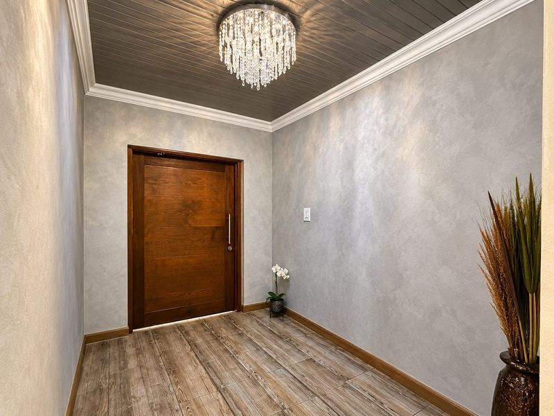 A modern, well-maintained entrance hall featuring a solid timber door, wood-look tiled flooring, and a decorative ceiling with crown molding.