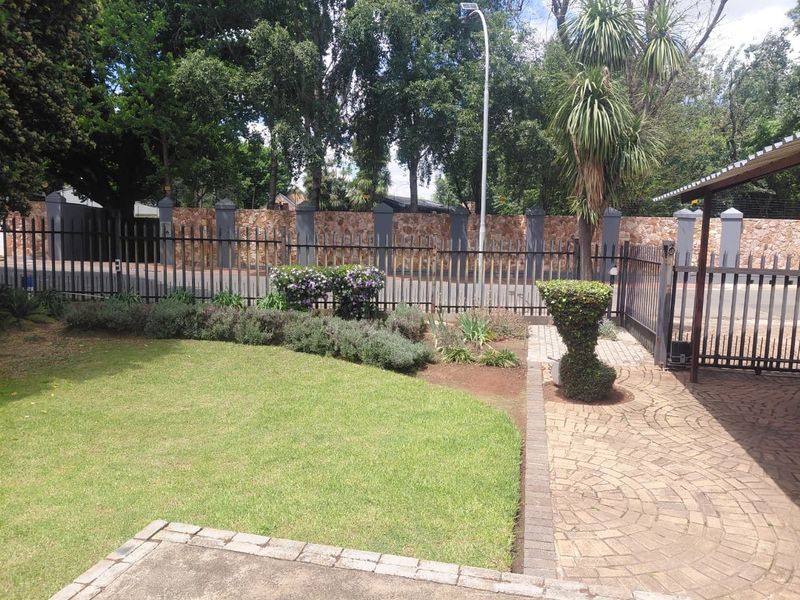Front exterior view featuring a well-maintained garden, paved driveway, and secure metal perimeter fencing with a stone boundary wall.
