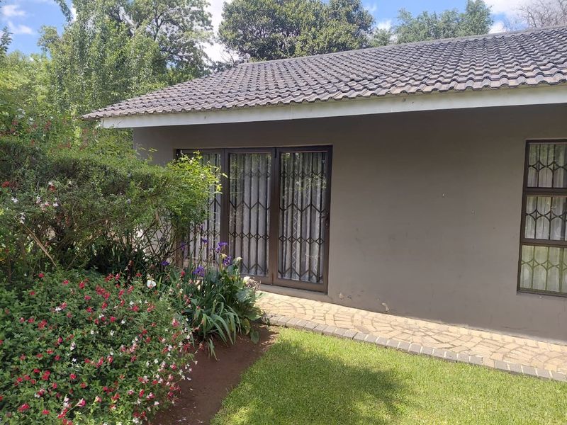 Rear exterior view of the property featuring a tiled roof, sliding glass doors with security gates, and a paved walkway leading through the garden.