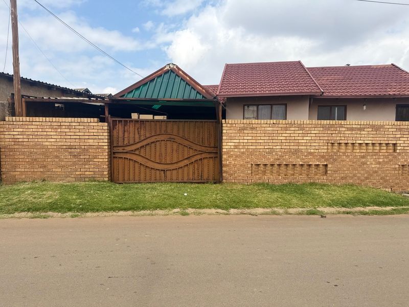 Front view of the property featuring a face brick boundary wall, a metal driveway gate, and a covered carport area.
