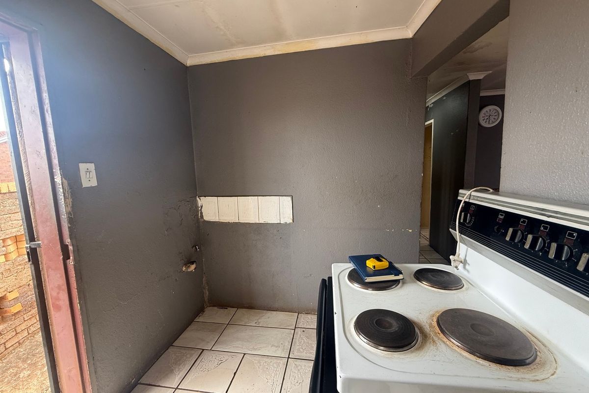 A small kitchen area featuring tiled flooring and an electric stove, currently requiring cosmetic updates and wall repairs.