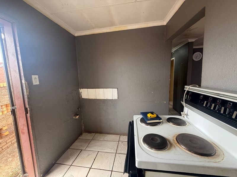 A small kitchen area featuring tiled flooring and an electric stove, currently requiring cosmetic updates and wall repairs.