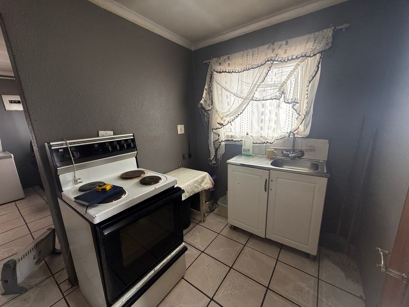 A compact kitchen area featuring a freestanding electric stove, stainless steel sink, and tiled flooring, offering potential for modernization and improved layout.