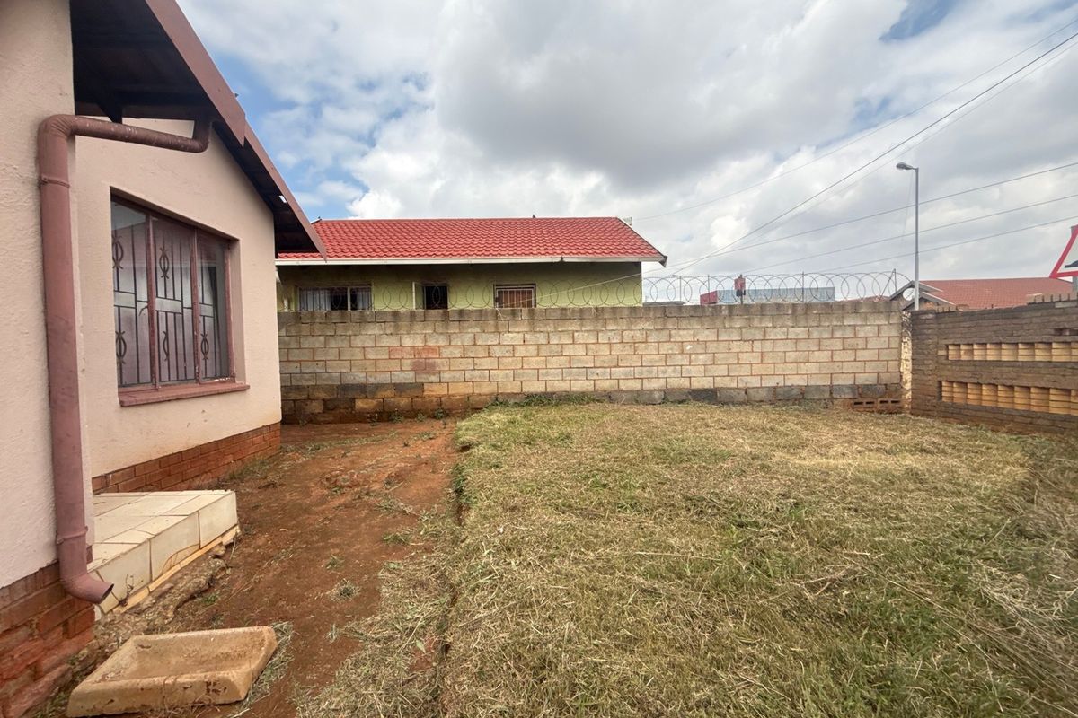 Rear garden area featuring a concrete block boundary wall with security razor wire and a small tiled step leading from the house.