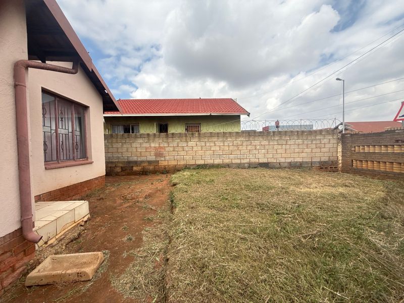 Rear garden area featuring a concrete block boundary wall with security razor wire and a small tiled step leading from the house.