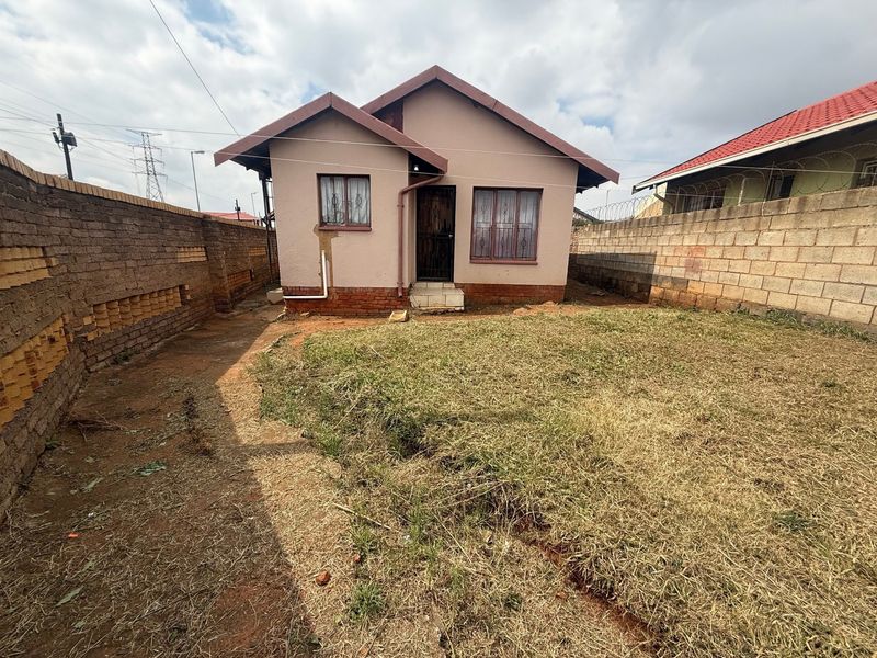 Rear view of a detached house featuring a brick boundary wall, security bars on windows, and a private garden area.
