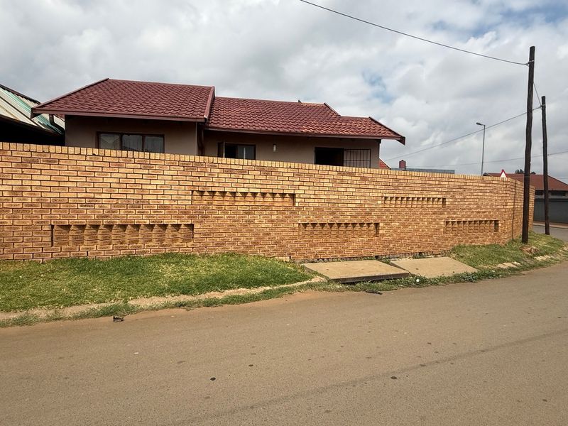 Street view of the property featuring a prominent brick boundary wall and a tiled roof house structure.