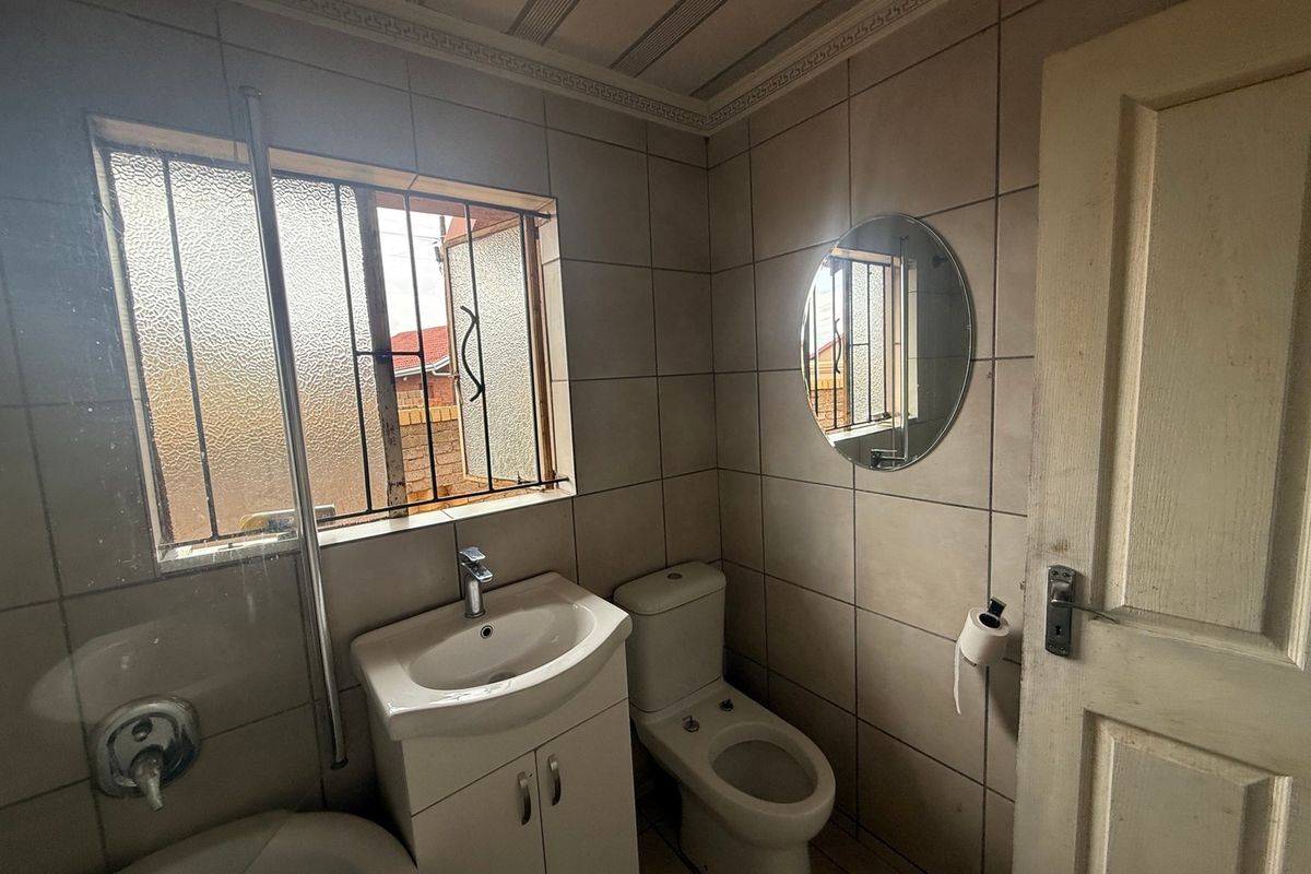 A functional bathroom featuring tiled walls and floors, a vanity basin, and a toilet, with security bars on the window.