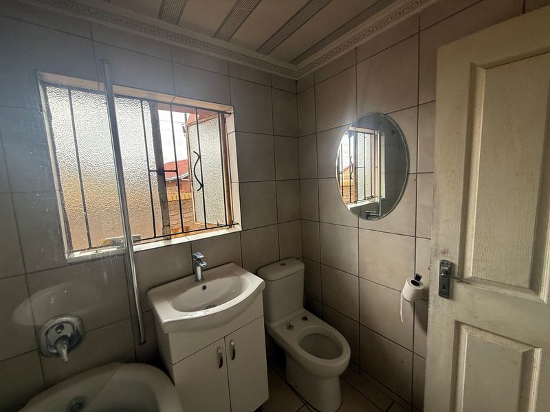 A functional bathroom featuring tiled walls and floors, a vanity basin, and a toilet, with security bars on the window.