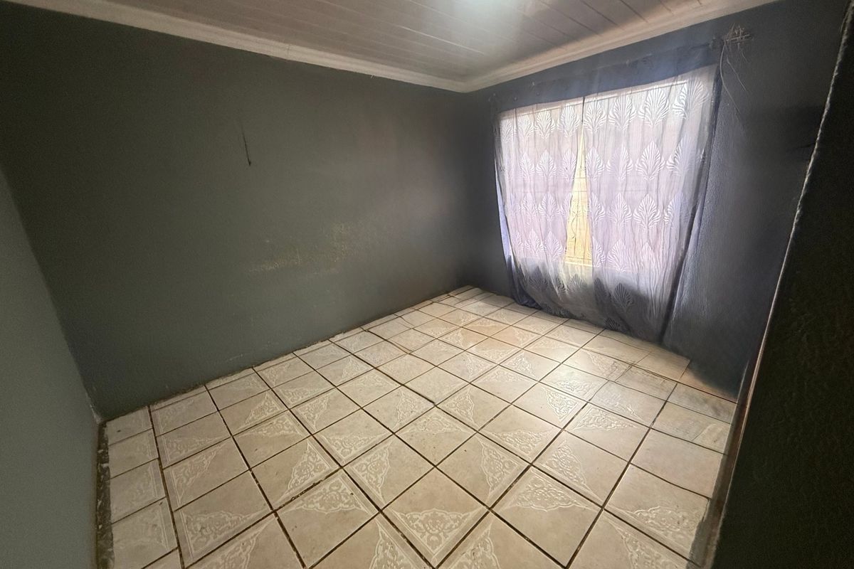 An empty bedroom featuring tiled flooring, a tongue and groove ceiling, and dark painted walls, ready for a fresh update.