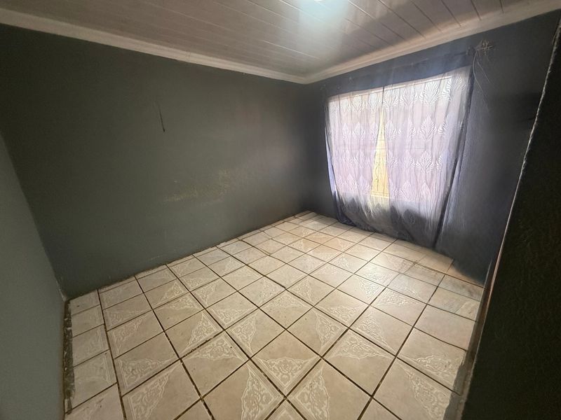 An empty bedroom featuring tiled flooring, a tongue and groove ceiling, and dark painted walls, ready for a fresh update.