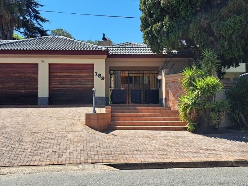 Front elevation of a residential property featuring a triple garage, paved driveway, and secure gated entrance with established garden landscaping.