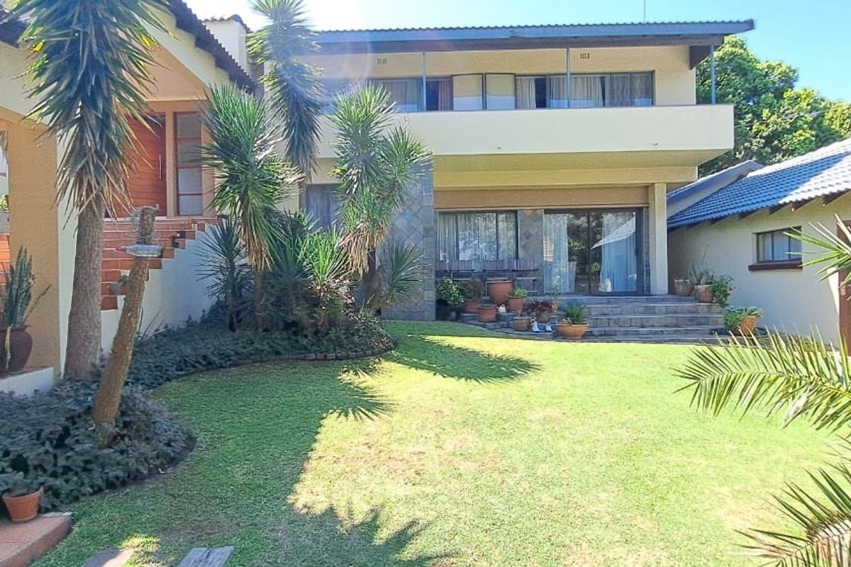 Spacious rear exterior view featuring a landscaped garden, tiled patio area, stone-clad accents, and a multi-level house structure with a balcony.