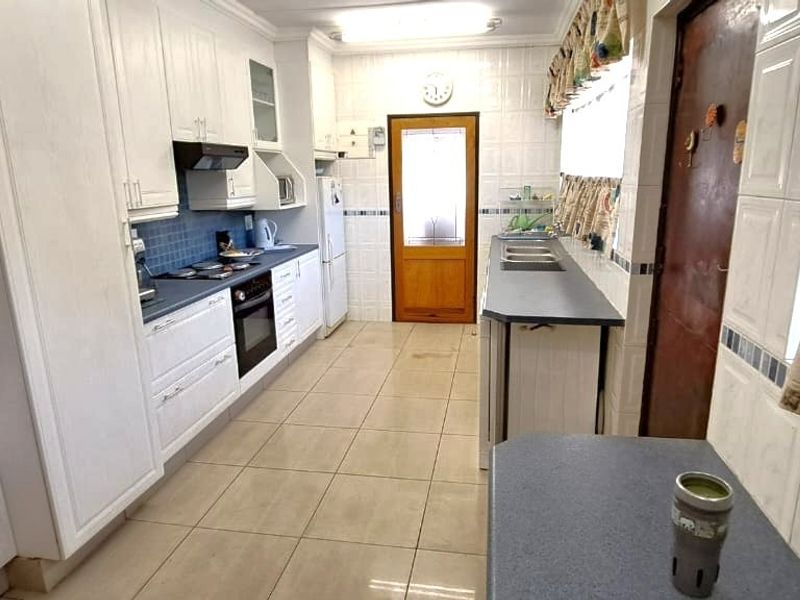 A functional kitchen featuring white built-in cabinetry, dark countertops, tiled walls, and flooring, providing a practical workspace with integrated appliances.