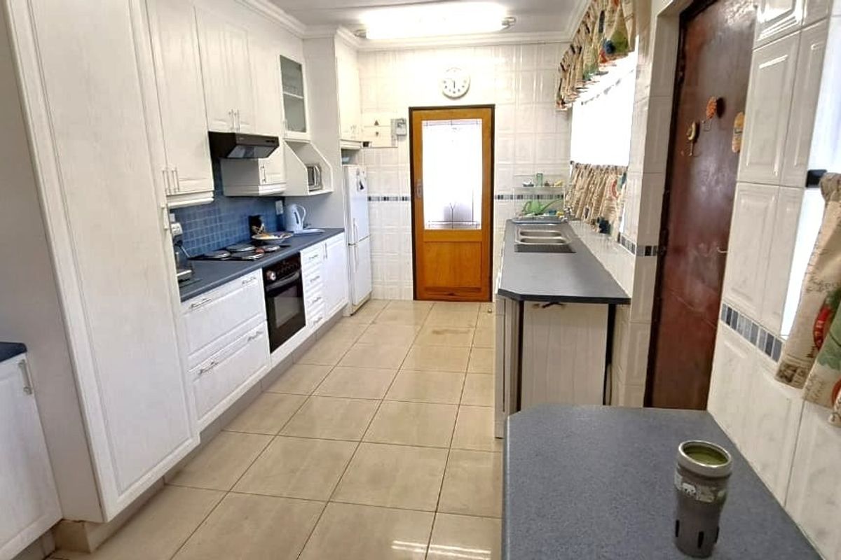 A functional kitchen featuring white built-in cabinetry, dark countertops, tiled walls, and flooring, providing a practical workspace with integrated appliances.