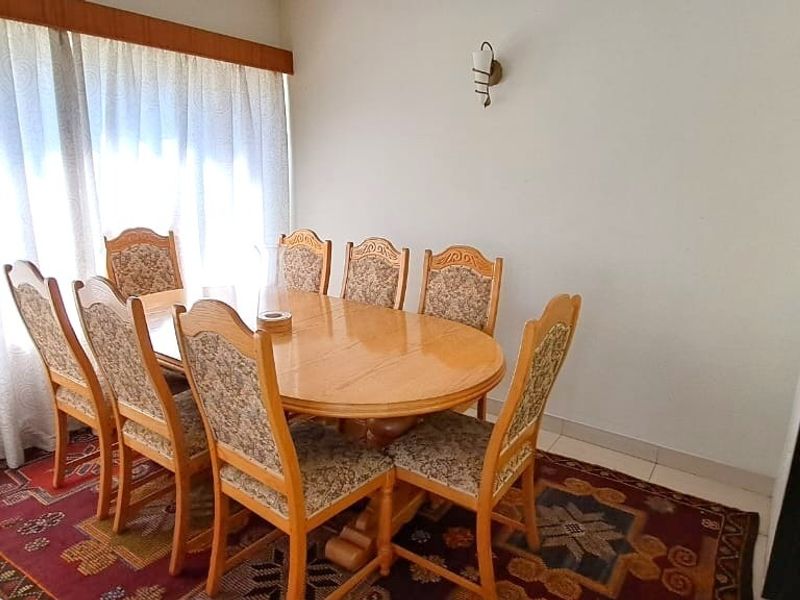 A functional dining room featuring a large window with curtain rails and a wall-mounted light fixture.