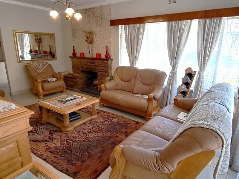 A spacious living room featuring a classic brick fireplace with a stone accent wall, tiled flooring, and large windows allowing for natural light.
