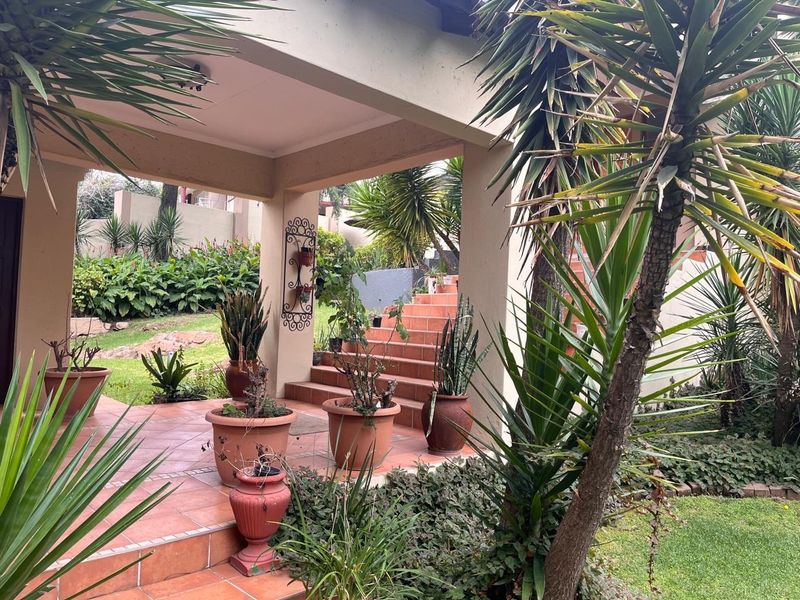 A covered outdoor patio area featuring tiled flooring and steps leading into a landscaped garden setting.