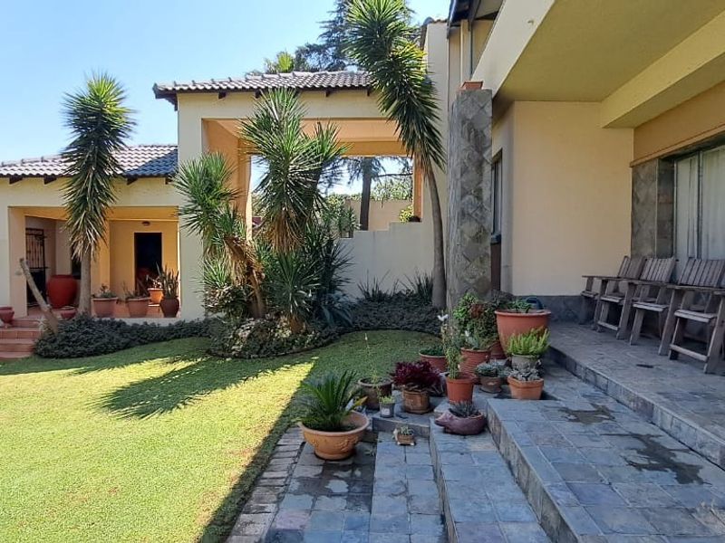 A spacious rear garden featuring a tiled patio area, stone-clad pillars, and a covered walkway connecting sections of the home.