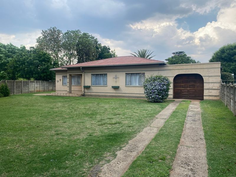 Front view of a single-story house featuring a brick facade, metal roof, attached garage, and a spacious front lawn with a concrete driveway.