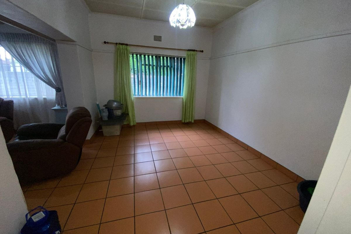 A spacious, empty living area featuring terracotta-style floor tiles, neutral walls, and a window with vertical blinds, offering a blank canvas for renovation.