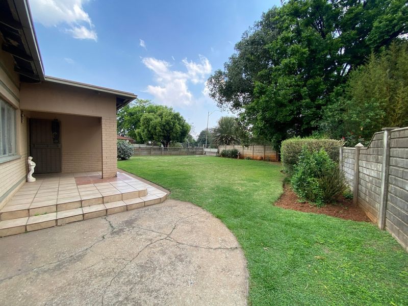 A spacious rear garden featuring a covered tiled patio, concrete paving, and established lawn enclosed by precast concrete boundary walls.