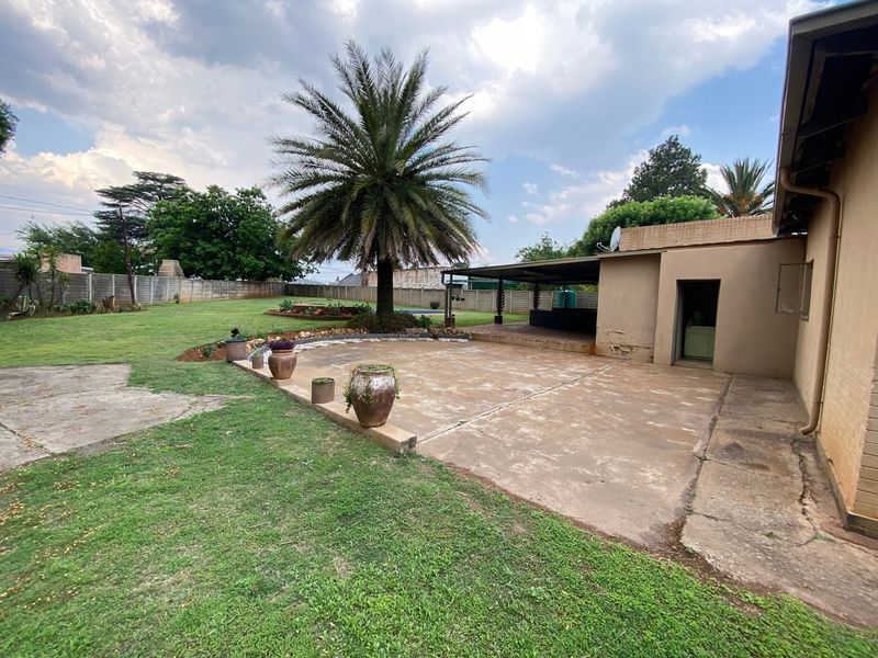 Spacious rear garden featuring a large concrete patio, covered outdoor entertainment area, and established palm tree, enclosed by a precast boundary wall.