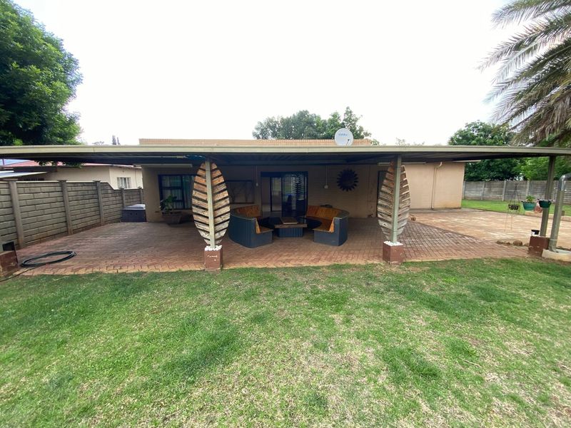 Spacious covered outdoor patio featuring brick paving and a metal roof structure, overlooking a private garden area.