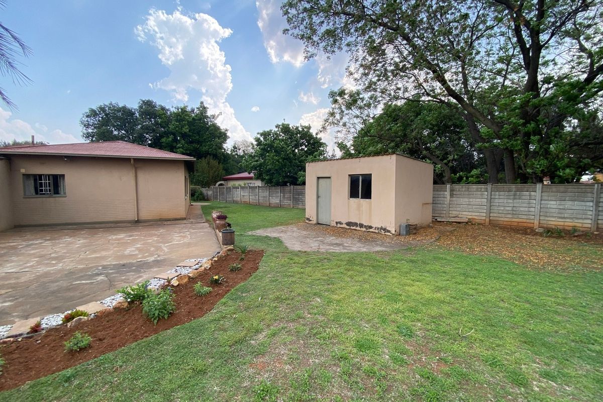 Spacious rear garden featuring a concrete patio, a detached outbuilding, and perimeter boundary walling under a clear sky.