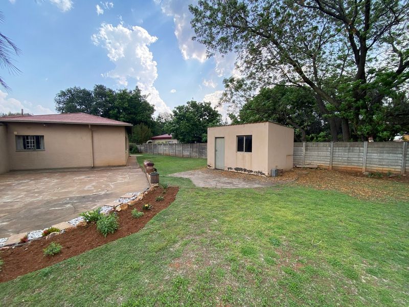 Spacious rear garden featuring a concrete patio, a detached outbuilding, and perimeter boundary walling under a clear sky.