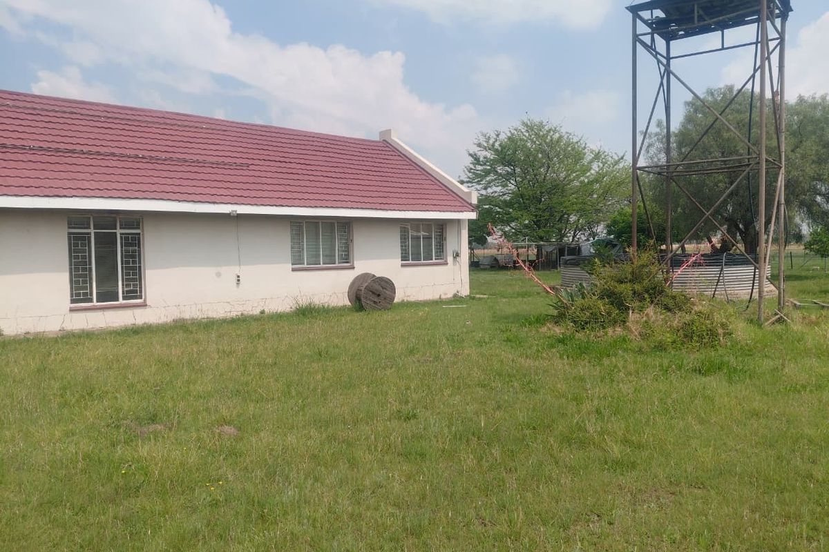 Rear view of the property featuring a metal water tank stand, corrugated water tank, and tiled roof structure set within a large garden area.