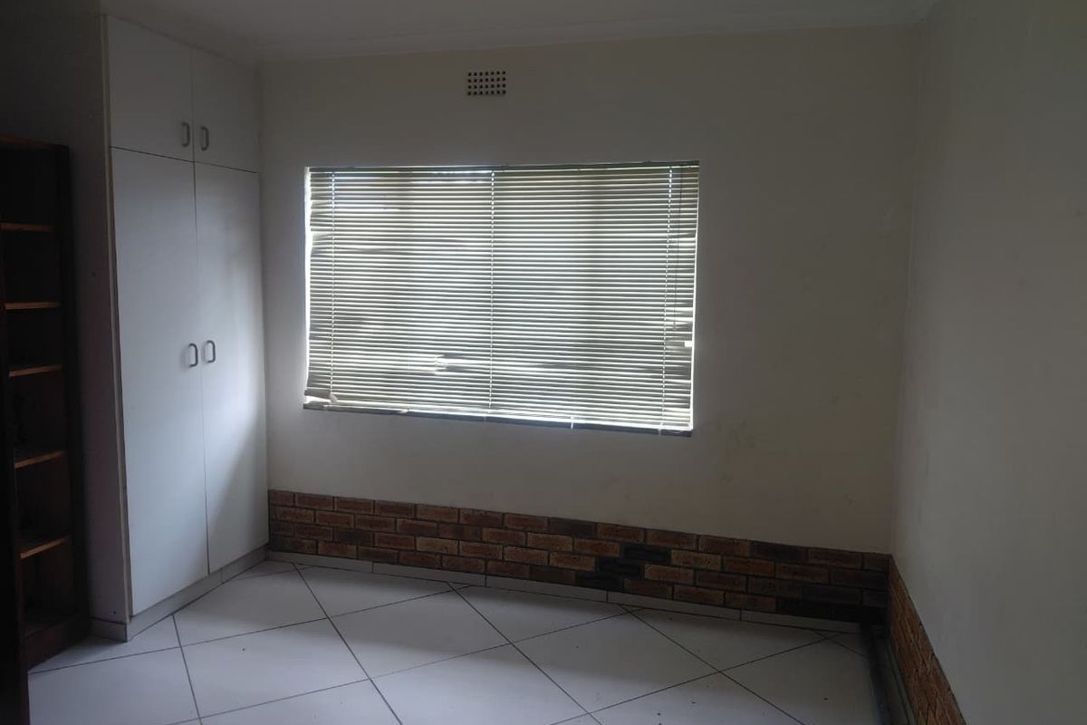 A vacant bedroom featuring tiled flooring, built-in cupboards, and a window with venetian blinds, offering a neutral canvas for personalization.