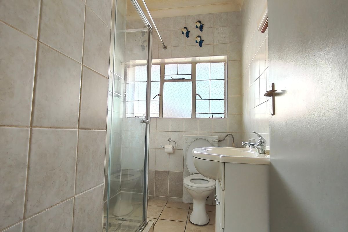 A compact bathroom featuring a shower enclosure, toilet, and vanity basin with tiled finishes throughout.