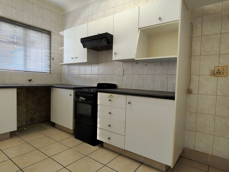 A dated kitchen featuring white cabinetry, a freestanding stove, and tiled finishes, currently vacant and in need of cosmetic updates.