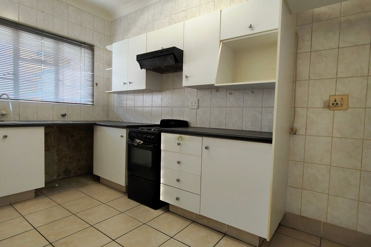 A dated kitchen featuring white cabinetry, a freestanding stove, and tiled finishes, currently vacant and in need of cosmetic updates.